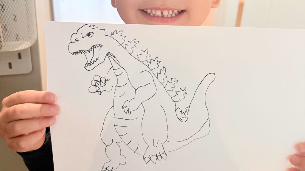 Child proudly holding a dinosaur drawing made on paper